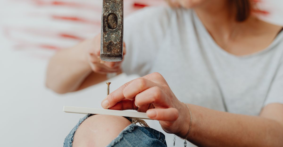 Woman uses a hammer and nail for DIY home improvement project.